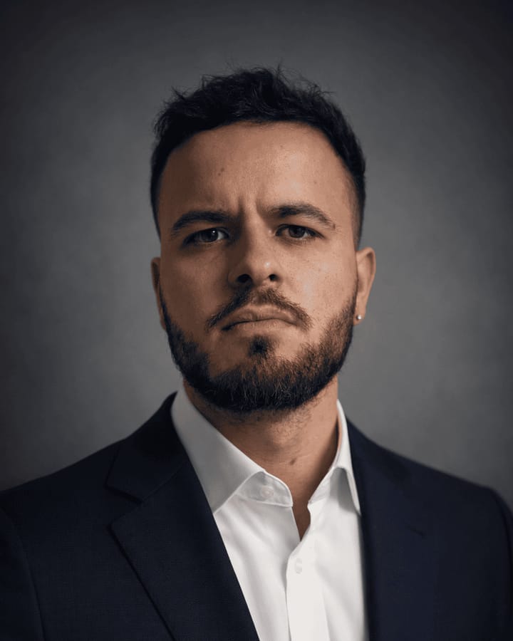 Retrato de Víctor Rocamora: hombre de pelo corto oscuro y barba, con americana azul marino y camisa blanca, sobre fondo gris oscuro